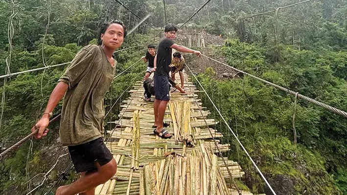 --- # Burnt, Flooded, Rebuilt Again — Beging's Hanging Bridge Refuses to Die Every time the river takes it away, the people of Beging come back and rebuild it with their own hands. That, in itself, says everything about this village. **A Bridge That Holds a Village Together** Deep in Arunachal Pradesh's Siang district, the village of Beging depends on a humble bamboo-and-rope hanging bridge called *Pebing Ie'am* to stay connected to the rest of the world. This bridge — swaying over the river, built without government contracts or heavy machinery — is the only link between Beging and Boleng, the Siang district headquarters. Students cross it to reach school. Farmers carry their produce over it. Elders make their way to hospitals on the other side. Without it, Beging is, for all practical purposes, cut off. **Six Decades of Survival** The story of Pebing Ie'am is not a short one. Village elders say the bridge was first constructed back in 1964. It stood for decades as the village's lifeline, until the floods of 2000-01 tore it away. But Beging didn't wait for a government order. The community rebuilt the bridge themselves, with support from the people of Dosing Rengo Lilleng village — a quiet, powerful act of solidarity that most official records probably never captured. That kind of resolve doesn't come from a policy paper. It comes from knowing exactly what's at stake. **Protest, Fire, and Another Setback** Then came June 2025. The bridge was reportedly burnt by protesters during an agitation against the Siang Upper Multipurpose Project (SUMP), and this happened in the presence of a magistrate and armed forces. Think about that for a moment — a bridge that generations built, reduced to ash, in full view of the authorities. Whatever the politics surrounding the SUMP agitation, what was lost that day was not just timber and rope. It was someone's route to a doctor, a child's path to school, an old man's connection to the market. **Coming Together, Again** Villagers have now come together once more to reconstruct Pebing Ie'am through their own efforts, demonstrating that same community spirit that has carried Beging through every crisis. Work is ongoing. And while there is no word yet about any government support stepping in, the people aren't waiting around. They never really have. **More Than Just a Bridge** There's something quietly remarkable about a community that rebuilds the same bridge three times across six decades — each time from scratch, each time without being asked. Pebing Ie'am is not just a structure. It is Beging's refusal to be forgotten, its insistence on staying connected, its testament that when the state looks away, a village can still look after itself. The river can break it. Fire can burn it. But it seems the people of Beging will simply build it again. --- **② ARTICLE TAGS** Beging village, Pebing Ie'am, hanging bridge, Siang district, Boleng, Arunachal Pradesh, bamboo bridge, community rebuild, SUMP protest, bridge fire, bridge reconstruction, traditional bridge, village connectivity, flood damage, 2025 protests, Siang river, remote village, community cooperation, indigenous infrastructure, North East India, rural connectivity, bridge repair, tribal community, community effort, village resilience, Arunachal news, Siang Upper Multipurpose Project, bridge destroyed, village bridge --- **④ SOCIAL MEDIA HASHTAGS** #BegingVillage #PebingIeam #ArunachalPradesh #HangingBridge #SiangDistrict #Boleng #CommunityResilience #BridgeRebuild #NorthEastIndia #ArunachalNews #SUMP #VillageConnectivity #TraditionalBridge #BambooAndRope #RuralArunachal #AbotaniTV #SiangRiver #PeoplesPower #TribalResilience #RebuildingTogether